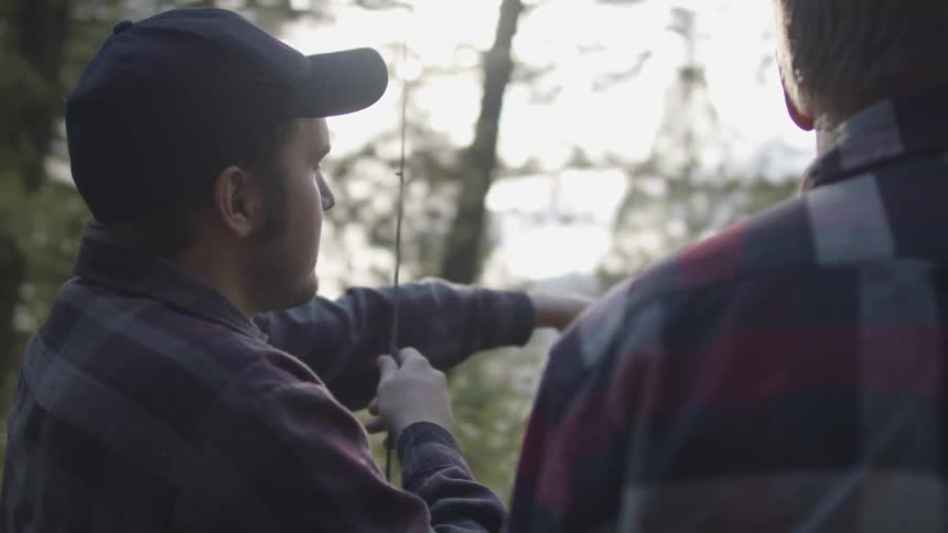 Father and son standing in the forest with fishing rods at sunset
