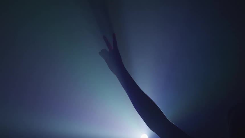A person raises the piece sign in front of the spot light