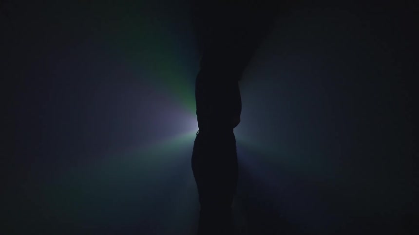 The silhouette of a female dancer spinning in front of a spotlight in a dark room
