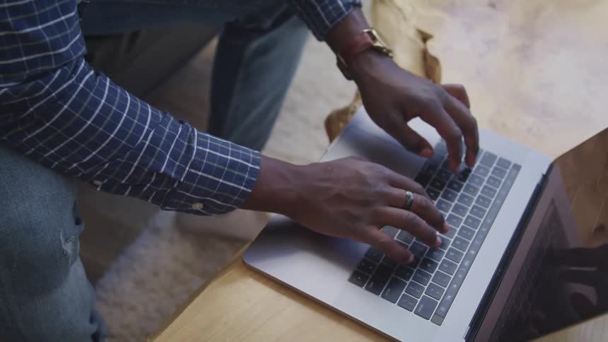 Close up of the hands of a person typing on the keyboard of a laptop over a table in a room