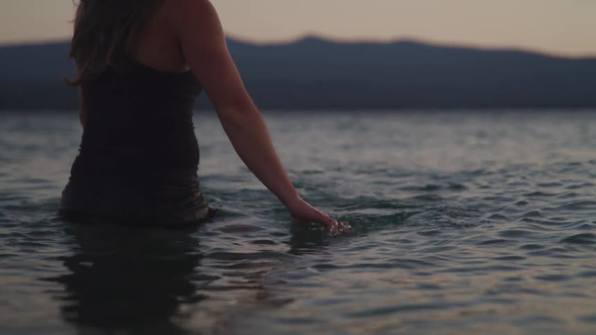 A woman moves her arms in the water as she stands in a lake