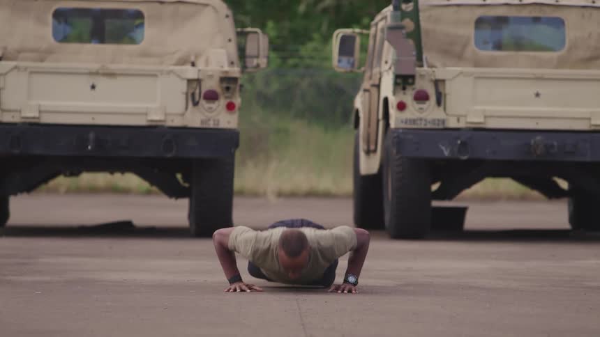 Soldier doing push ups in front of armored vehicles parked in a yard outdoors