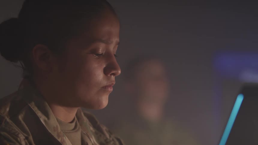 A uniformed soldier looks at a computer monitor and back down to type