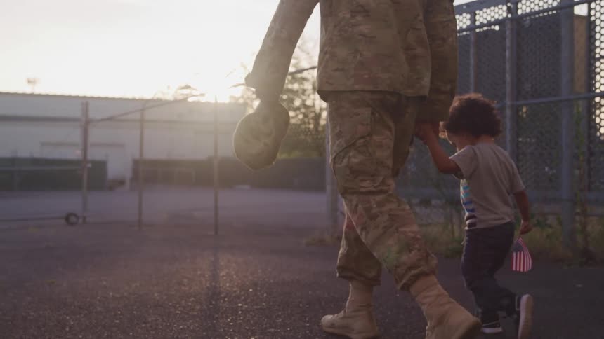 American soldier walking on the yard holding hands with his kid at sunset