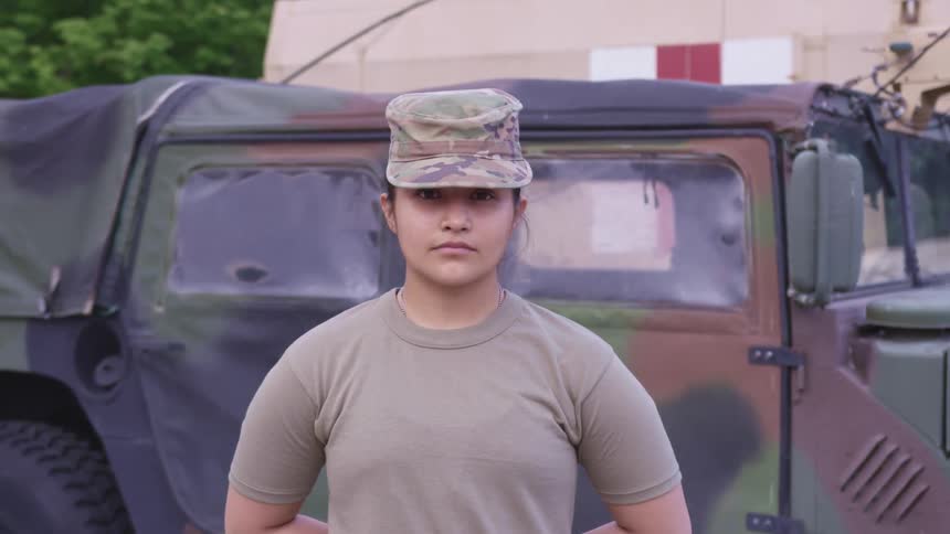 A female soldier stands at attention outside while posing for a portrait