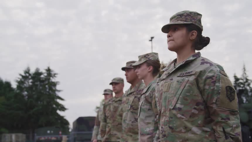 A group of soldiers stand in a line and slowly turn around and wait at attention
