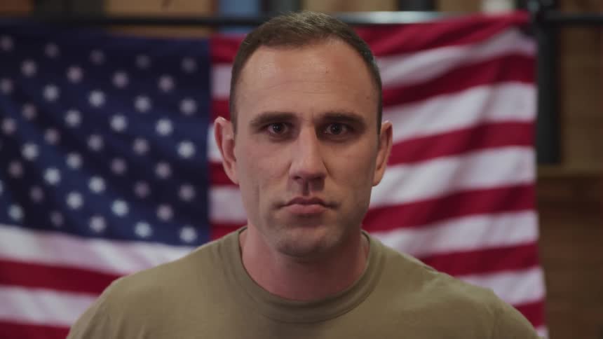 American army soldier standing in front of the american flag looks up at the camera