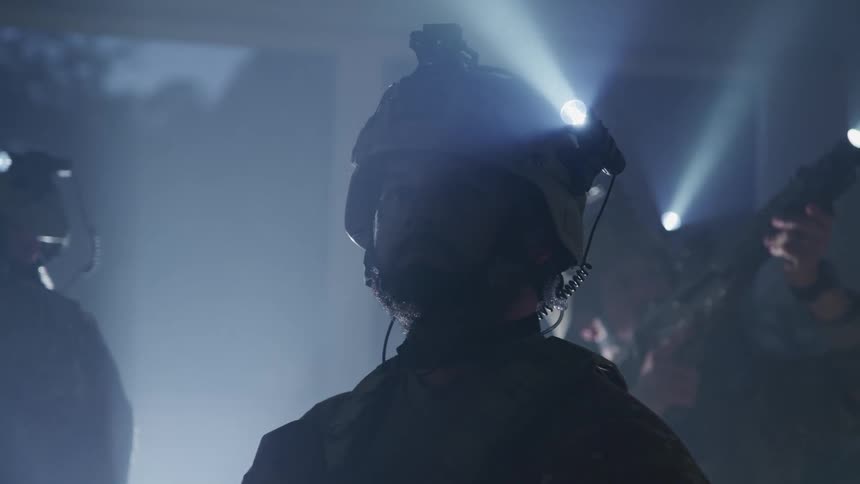 Three men with military uniforms and helmets with flashlights in a room with one of the men pointing a rifle