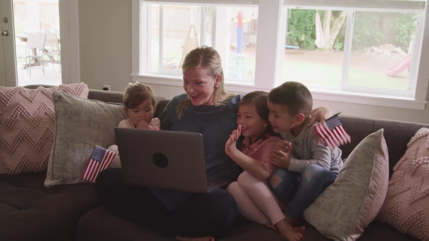 A woman two girls and a boy sitting on a couch video chatting on a laptop