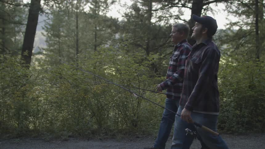 A pair of men carrying fishing poles walk together along a road path