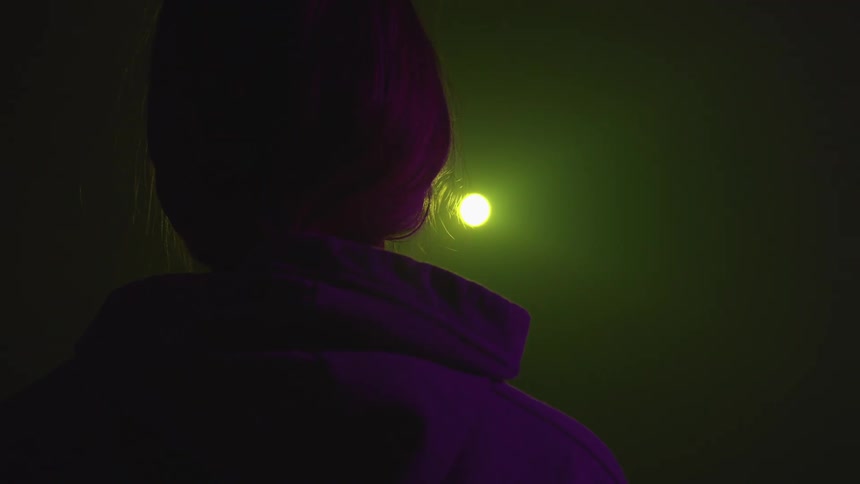 A woman faces a light beam and changing colors