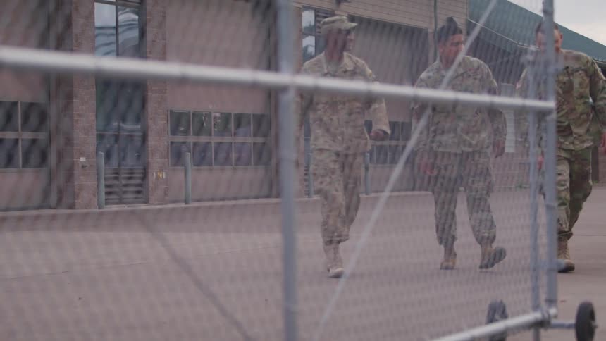 Three soldiers walk across a compound as they talk