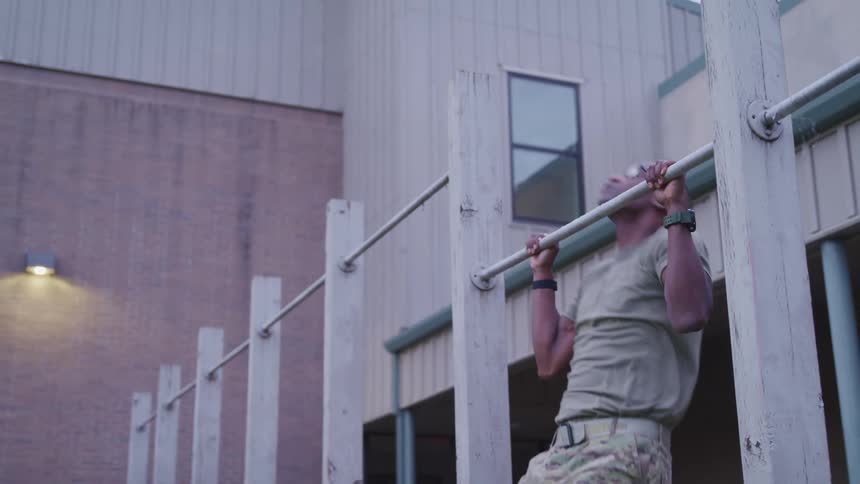 American soldier doing bar workout in the yard near a building