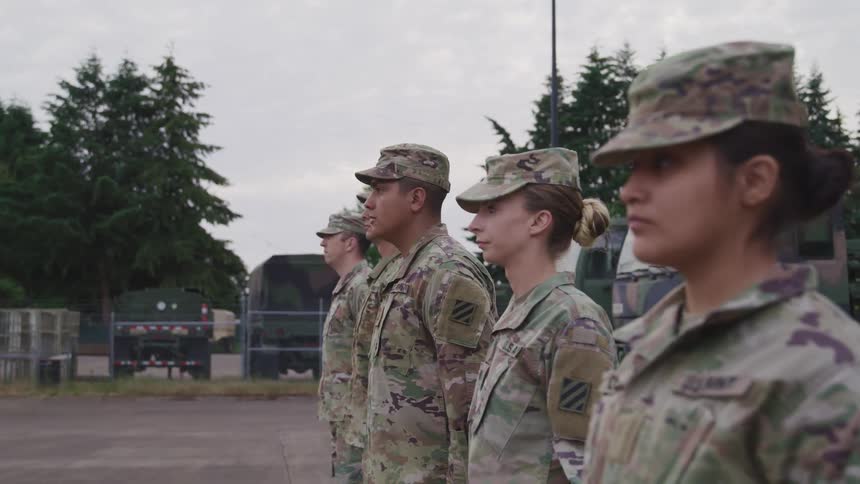 A group of male and female soldiers in uniform stand in a row while at attention