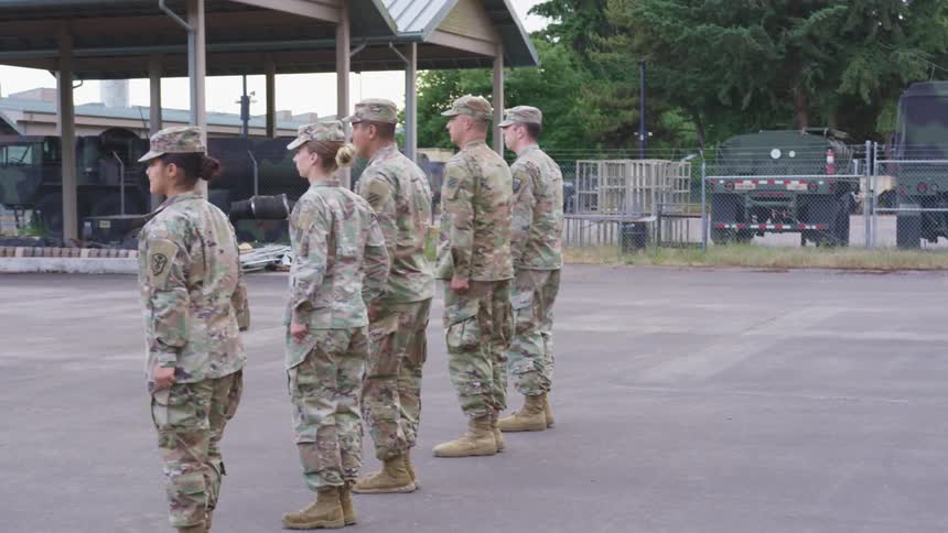 Soldiers in military uniforms lining up and turning with vehicles trees the sky and clouds in the background