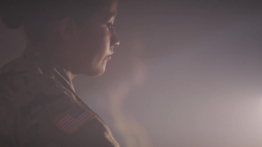 A woman in military uniform works in the light and glow of a computer