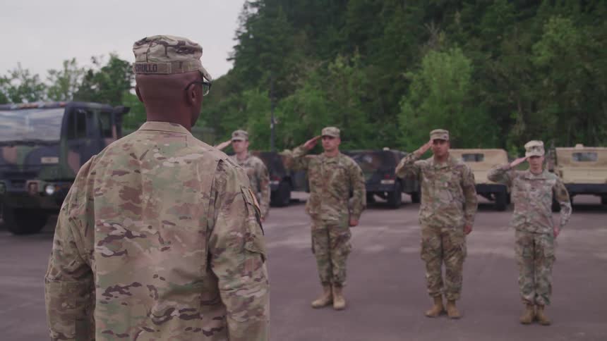 Us army troops standing in front of their captain performing a salute outdoors during the day