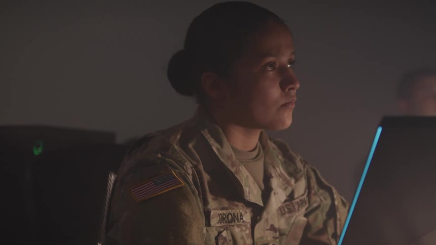 Young military woman in army uniform working on a computer in a dimly lit room
