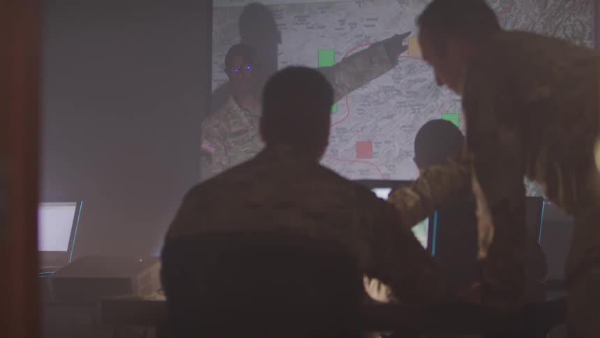 A soldier goes over a map projected onto a screen for a room full of other soldiers