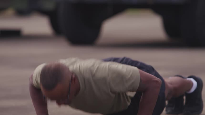 A man performs pushups in a parking lot during the day