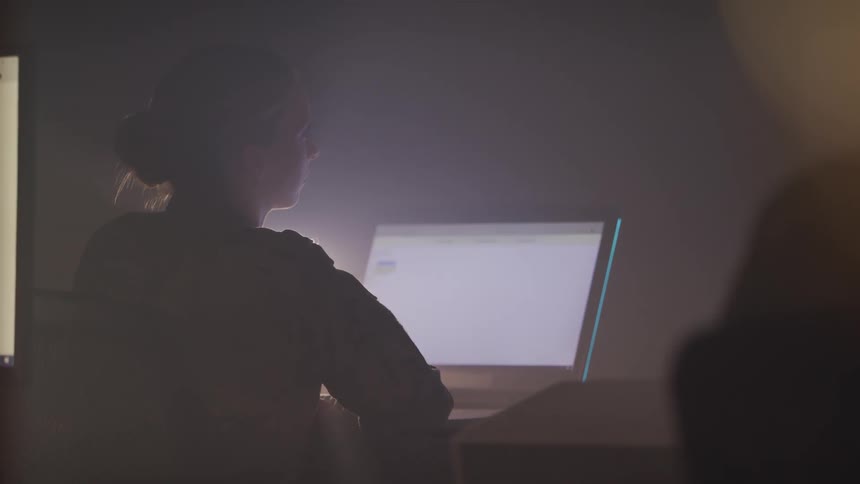 A woman in a military uniform sitting on a chair at a desk with a laptop