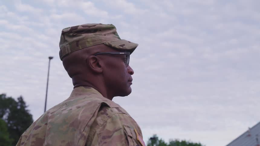 A uniformed soldier stands outside and looks off into the distance