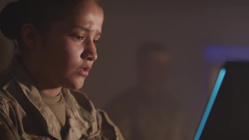 A woman in military uniform looks anxious as she works at a computer