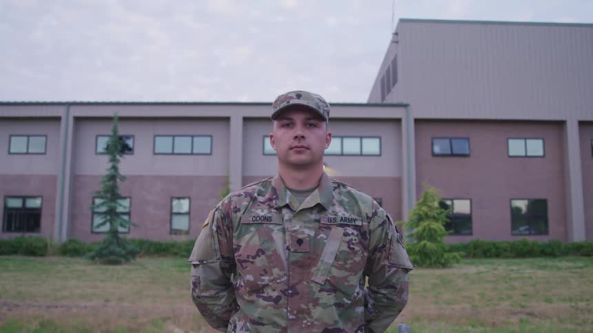 A man in a military uniform standing and staring with a building the sky and clouds in the background