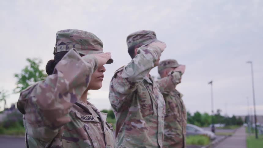 Soldiers in camouflage throw up a salute in unison as they stand on a sidewalk