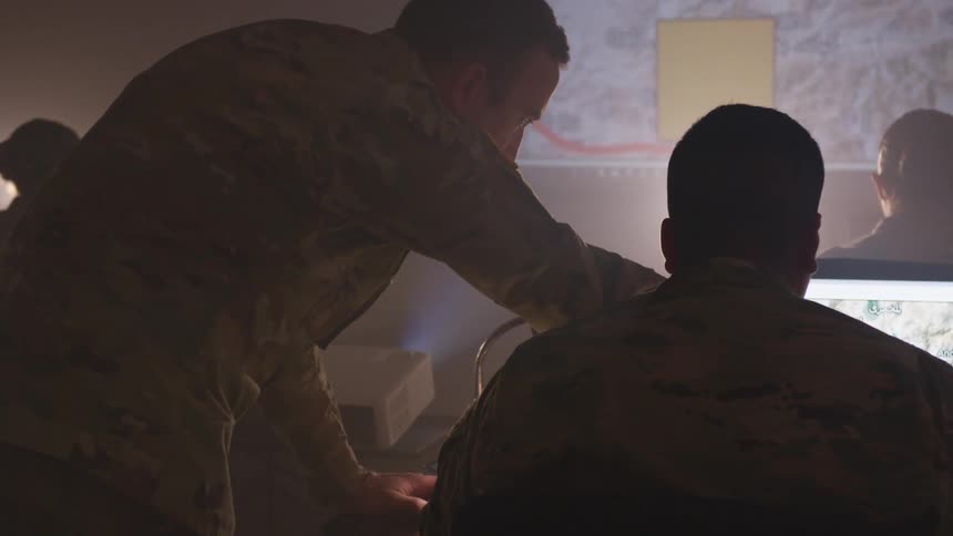 Soldiers in camouflage uniforms looking at maps on a computer monitor