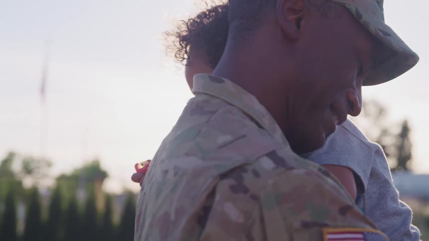 African american soldier smiles while holding son in his arms outdoors