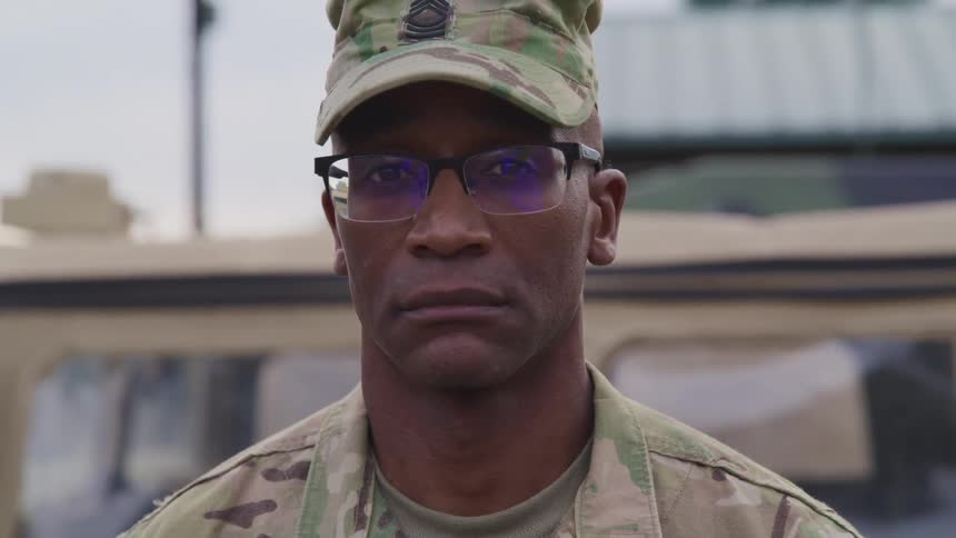 A uniformed soldier poses in front of a military jeep