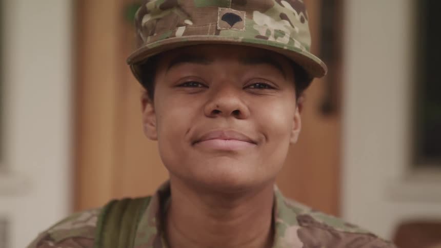 A woman in a military outfit slowly looks up at the camera while subtly smiling