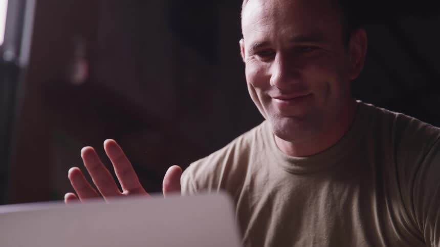 A man smiling and waving at a laptop