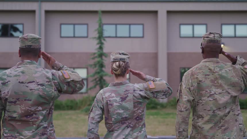 Soldiers in military uniform saluting with a building grass and a tree in the background