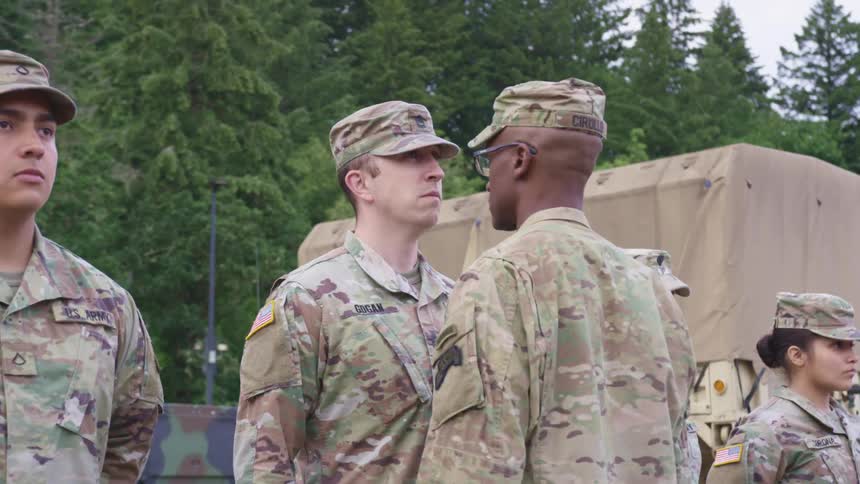 Soldiers stand in a line as an officer walks up and stares at one of the men