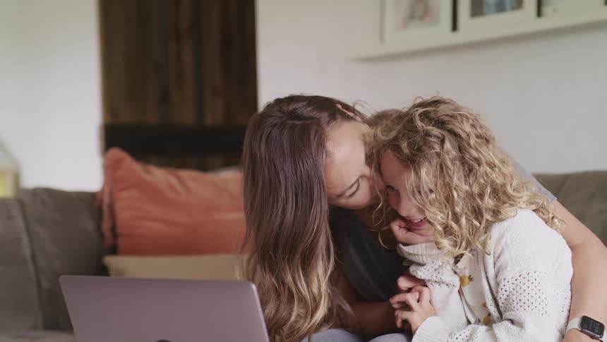 A woman and a girl sitting on a couch video chatting on a laptop