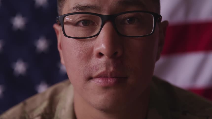 A young man in front of an american flag lifts his head up and looks straight ahead