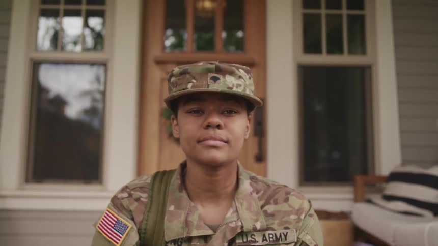 Young female american soldier sitting in the doorsteps at home looking at the camera