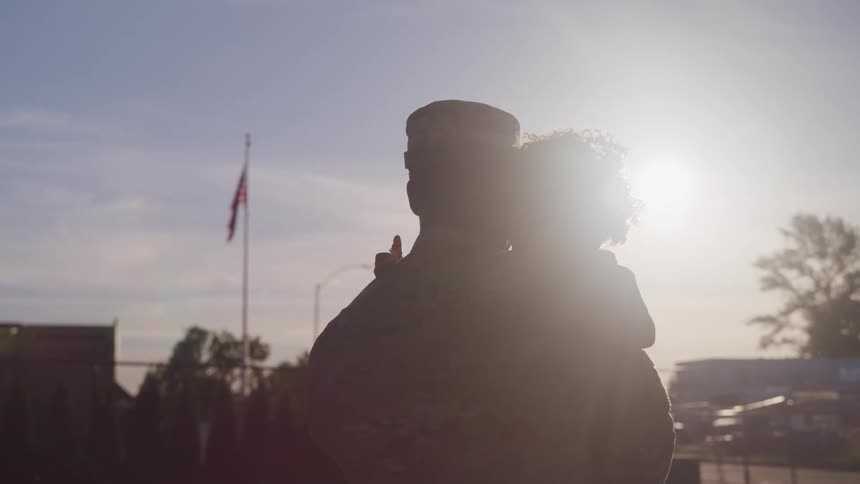 Silhouette of an american soldier holding his daugther in front of the sun
