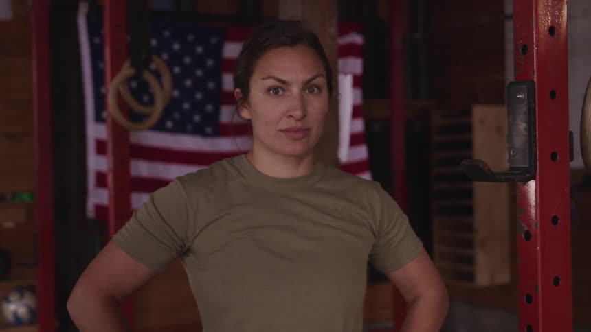 A woman standing and staring with exercise equipment and an american flag in the background