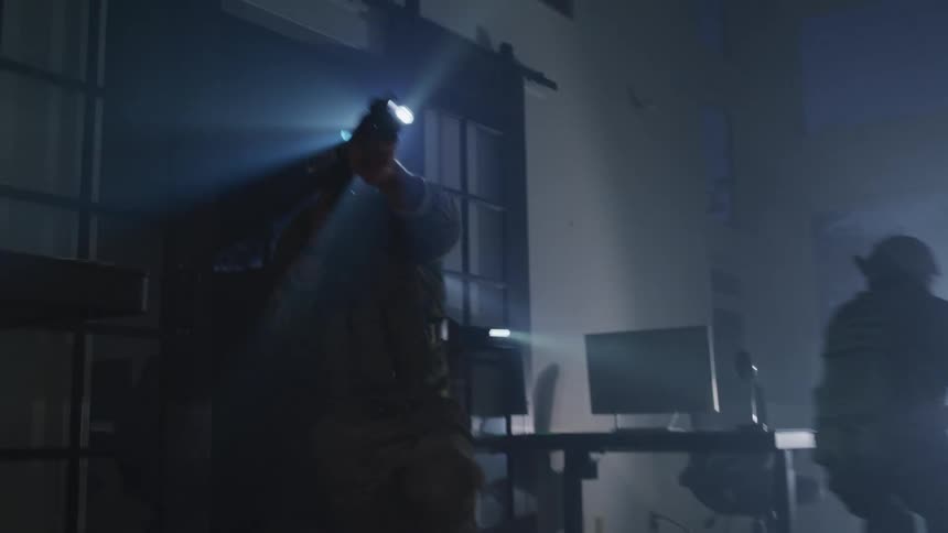 A group of armed soldiers quickly enter a dimly lit office at night