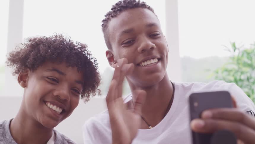 Young african american teenagers smiling and waving on a video call through a smartphone