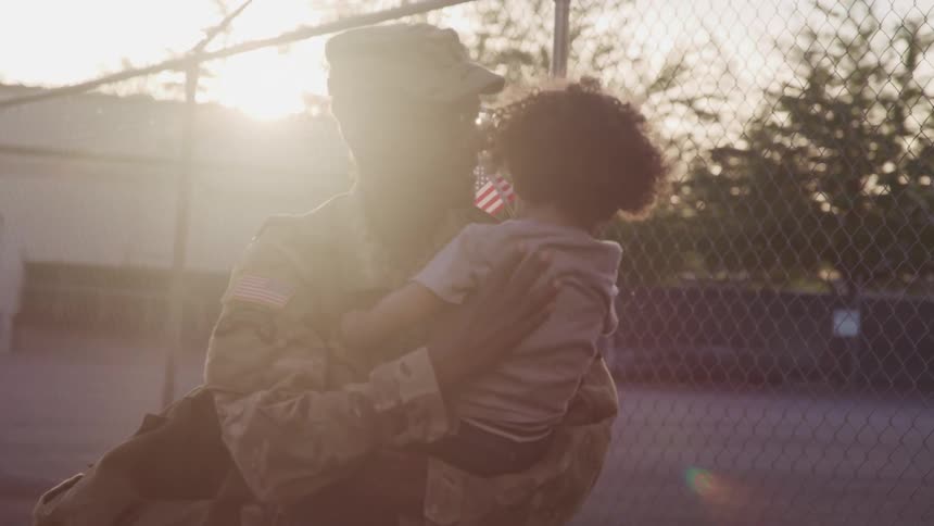 A uniformed soldier hugs his son in a parking lot