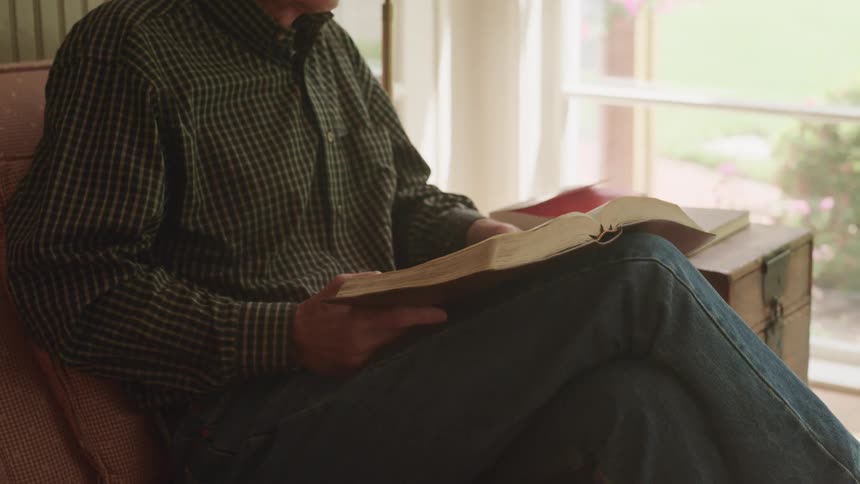 A man flips through a book while sitting with his legs crossed on a couch