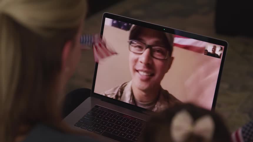 A soldier on a laptop waves to his wife and daughter as they video chat