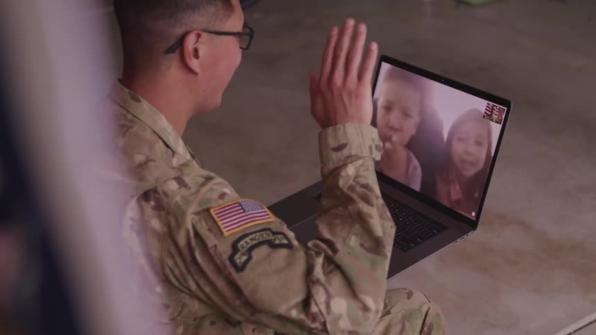 A soldier waves at his son and daughter as he video chats with them on a laptop