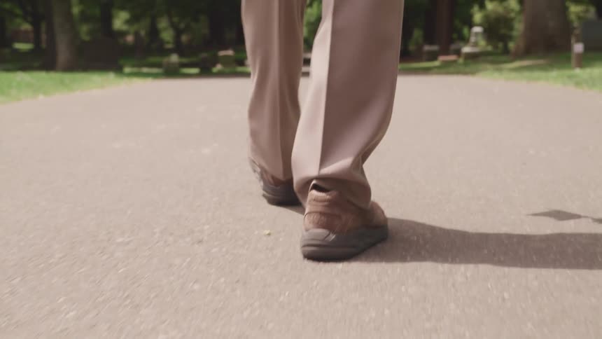 View of persons lower legs wearing tan dress pants and brown shoes walking on a road