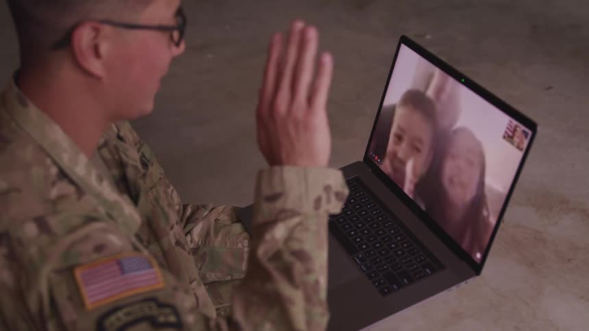 A man in a room with glasses and a military uniform video chatting on a laptop