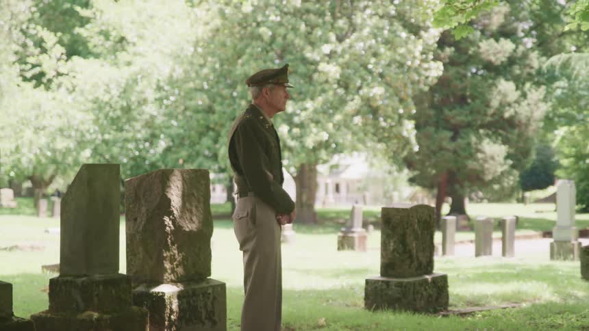 A veteran stands with his head bowed at a gravesite and then looks up